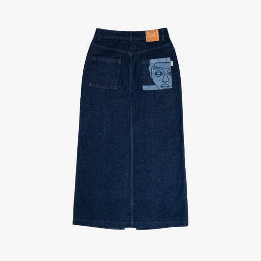 Jupe longue en jeans avec dessin au laser en plein sur le devant et la poche plaquée dos, droite au porté. Denim deep indigo rinse, 100% coton. Surpiqûres gros fil ton sur ton. Bouton et jacron cuir embossés, personnalisés.