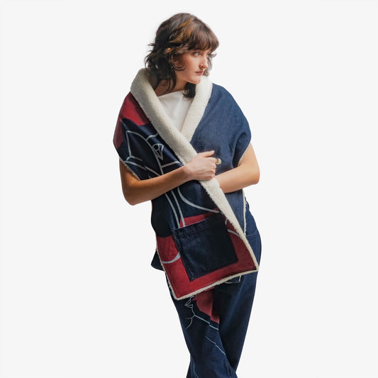Grande écharpe en denim bleu intense 100% coton, pensée pour offrir un porté poncho grâce à un bouton intégré. Son volume enveloppant procure chaleur et élégance, tandis qu’une grande impression en sérigraphie habille la moitié de sa surface. Les aplats rouges et lignes blanches rendent hommage à la fresque Avec Vous. Finitions soignées avec surpiqûres ton sur ton, bouton embossé et gomme personnalisée.
