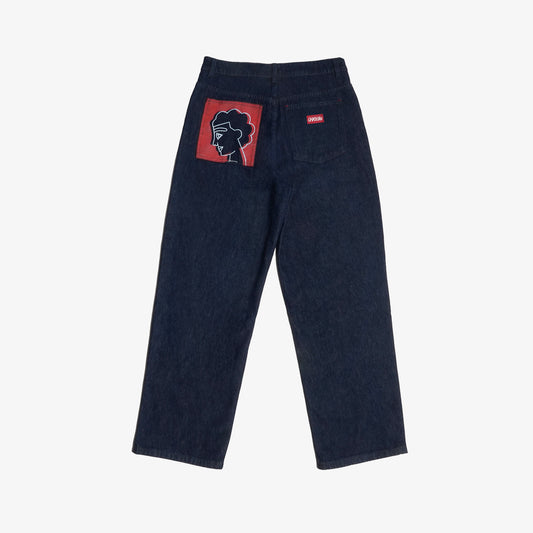 Jean brut confort en denim 100% coton, orné de sérigraphies placées sur trois poches carrées plaquées. Les aplats rouges et lignes blanches reprennent les codes graphiques de la fresque Avec Vous. Finitions avec surpiqûres ton sur ton, bouton embossé et gomme personnalisée.