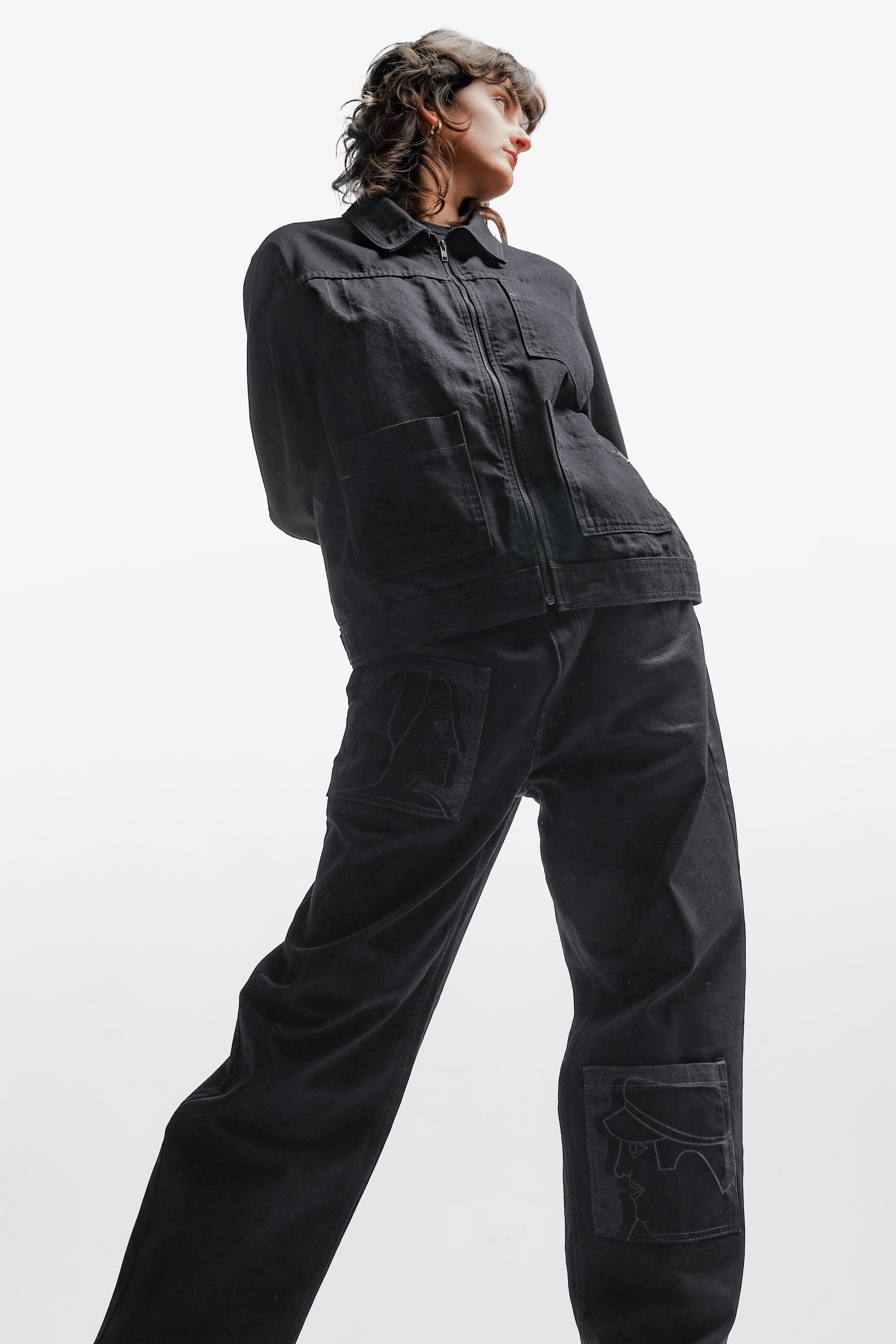 Veste en denim noir à l’inspiration workwear, revisitée avec une approche contemporaine. Son design structuré se distingue par trois poches carrées sur l’avant et des impressions au laser évoquant la fresque Avec Vous. Confectionnée en denim deep black rinse 100% coton, elle présente des surpiqûres en contraste gris, tandis qu’un jacron en cuir embossé noir apposé au dos signe son caractère unique.