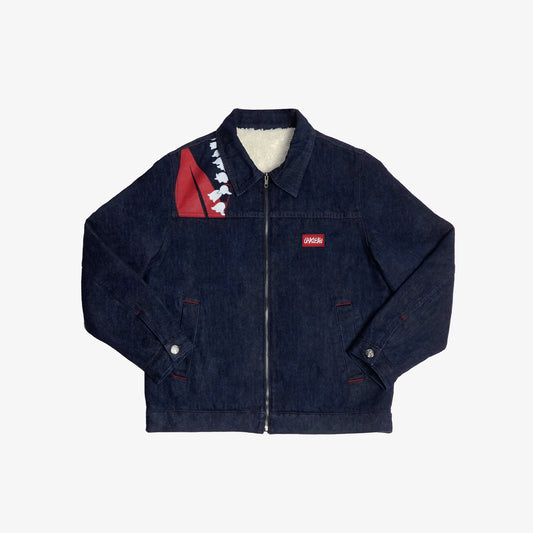 Veste en denim brut doublée en sherpa, alliant robustesse et confort. Ornée d’impressions sérigraphiques sur la poitrine et le dos, ses aplats rouges et lignes blanches s’inspirent directement de la fresque Avec Vous. Le denim bleu indigo 100% coton est sublimé par des surpiqûres ton sur ton, offrant un équilibre parfait entre design artistique et finition soignée.