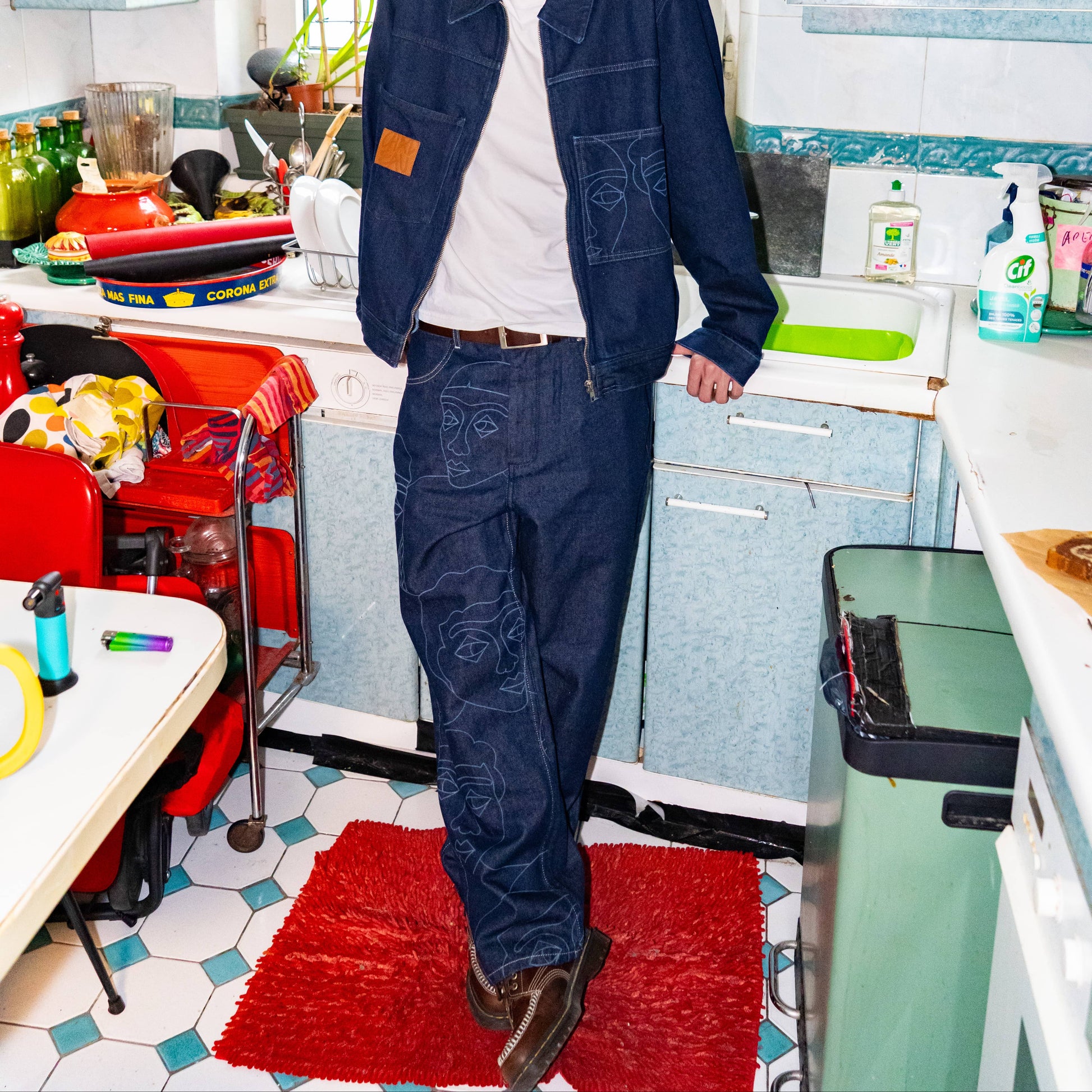 Veste trucker et jeans en denim indigo brut avec des imprimés de visages au laser sur tout la jambe droite et le. dos de la veste.