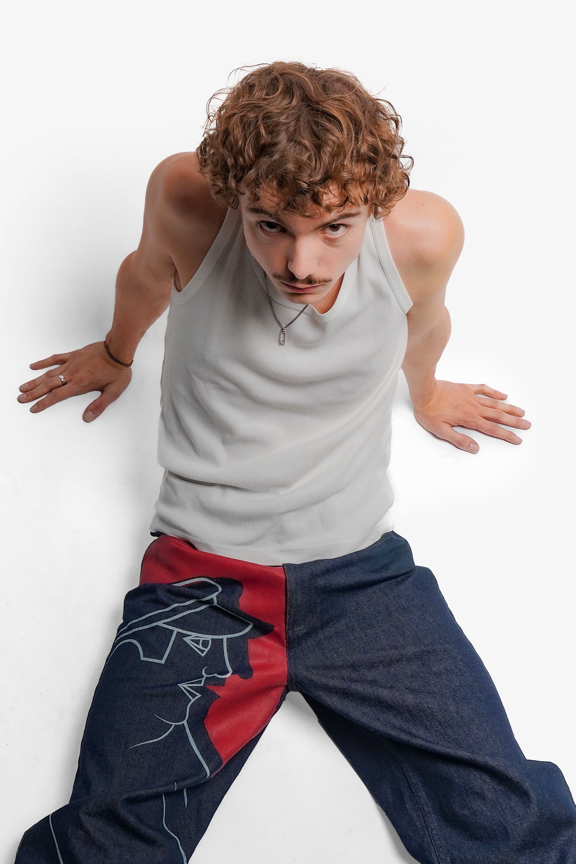 Une grande impression en sérigraphie recouvre toute la jambe droite, avec des aplats rouges et lignes blanches directement inspirés de la fresque Avec Vous. Confectionné avec des surpiqûres ton sur ton, il est signé d’un bouton et d’une gomme embossés et personnalisés.